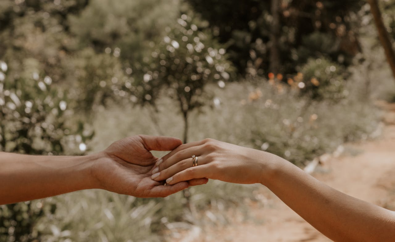 A close-up of two hands touching with a romantic ring outdoors.