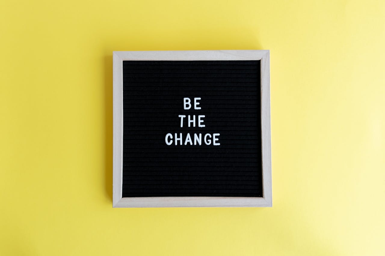 Minimalist letter board with 'Be The Change' quote on a vibrant yellow background.