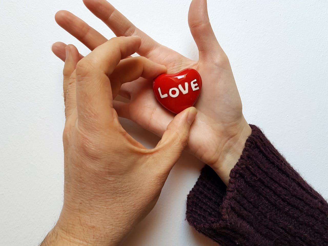 Two hands holding a red heart with the word 'love' on a white background.